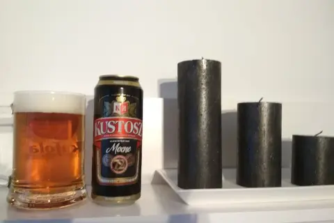 Kufel piwa i puszka Kustosz Mocne obok trzech czarnych świec.