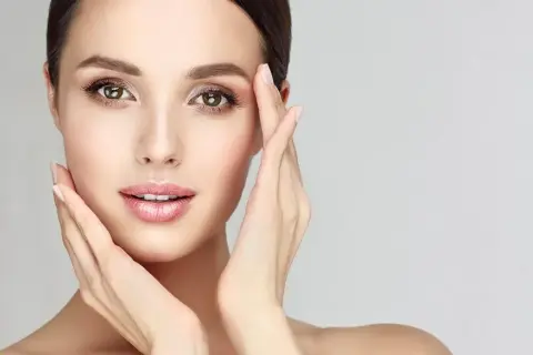 Visage de femme aux mains délicates caressant sa peau, évoquant un soin de nettoyage de peau parfait.