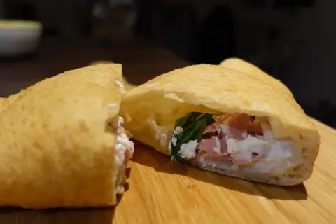 Une pizza frite napolitaine, garnie de ricotta, jambon et basilic, sur une planche en bois.