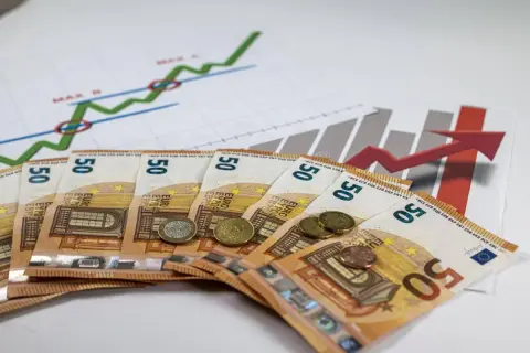 Euro banknoty i monety na tle wykresów wzrostu. Symbolizują inwestycje, zyski i potencjalną subwencję.