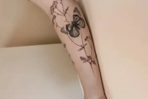 Un delicado tatuaje de mariposa y flores silvestres en un brazo, simbolizando la libertad y la belleza efímera.