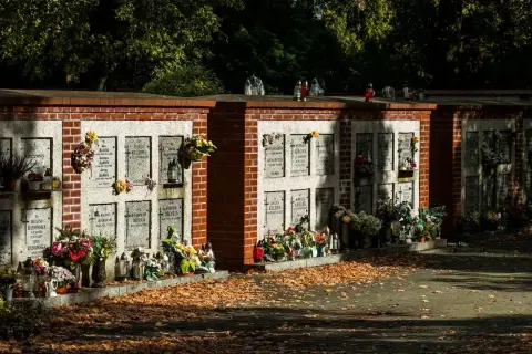 Kamienna ściana na urny z prochami, ozdobiona kwiatami i zniczami, otoczona jesiennymi liśćmi.