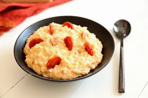 Un crémeux risotto chorizo, garni de rondelles de saucisse épicée, servi dans un bol noir avec une cuillère.