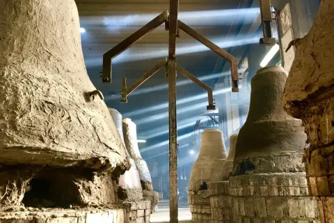 Forni antichi nel paese delle campane Molise, con raggi di luce che illuminano la polvere e le forme grezze delle campane in attesa di essere fuse.