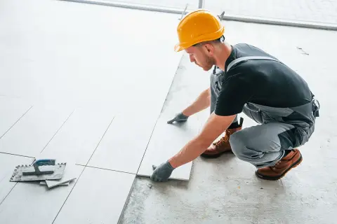 Fachowiec w żółtym kasku układa płytki. Zastanawiasz się, ile za metr płytek zapłacisz za taką pracę?
