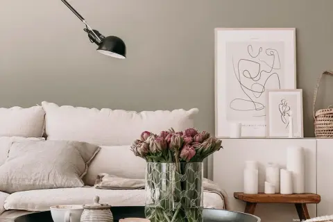 Gemütliches Wohnzimmer mit skandinavischen Wandfarben, einem Sofa mit Leinenkissen, Tulpen und minimalistischer Kunst.