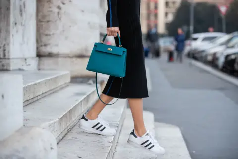 Scarpe da ginnastica bianche con strisce nere abbinate a un tubino nero e una borsa turchese.