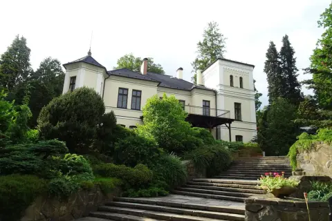 Ein hellgelbes Herrenhaus mit Turm und Balkon, umgeben von üppigem Grün und einer Steintreppe, in Opava, Tschechien.