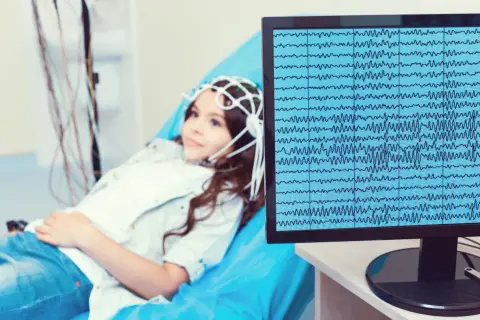 Dziewczynka z czepkiem do eeg leży na łóżku, a na monitorze widać zapis fal mózgowych.