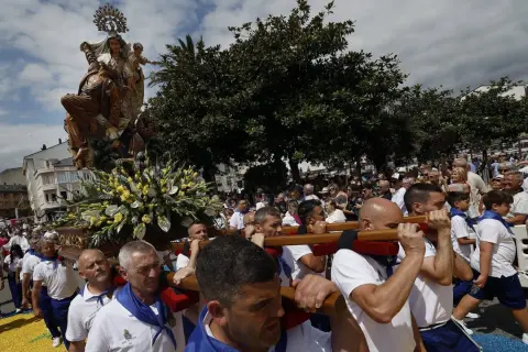 Procesión de la Virgen en las fiestas del Carmen de Foz. Hombres portan la imagen adornada con flores, mientras una multitud observa.