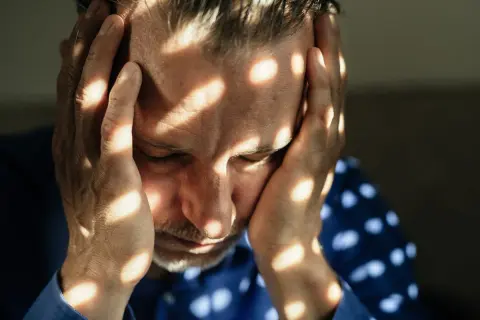Uomo con le mani sulla testa, illuminato da fasci di luce che creano un effetto di **blocco emotivo test**.