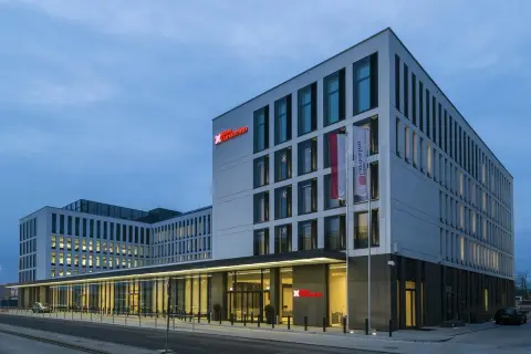 Nowoczesny budynek Hilton Garden Inn Kraków o białej fasadzie z czerwonym logo, z polską flagą przy wejściu.