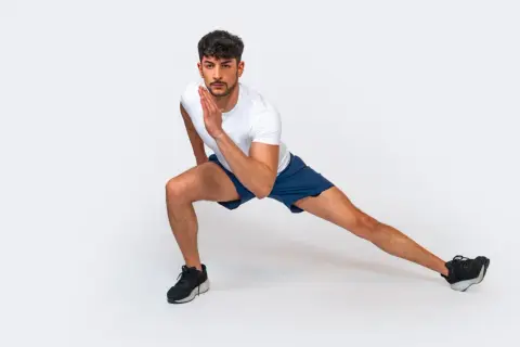 Uomo in posizione di affondo laterale, parte di una serie di 12 esercizi a corpo libero per allenarsi a casa.