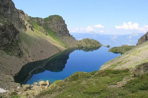 Le lac du Crozet, d'un bleu profond, reflète les montagnes escarpées et le ciel clair. Un paysage alpin paisible.