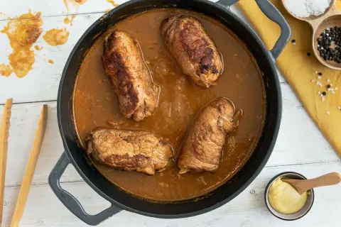 Herzhafte schweinerouladen nach omas rezept in dunkler Soße, bereit zum Servieren. Daneben Senf, Salz und Pfeffer.