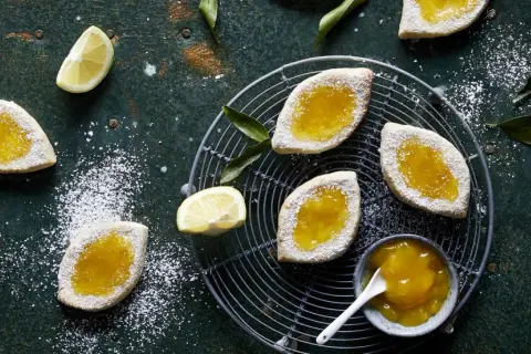 Italienische Kekse mit Lemon Curd, bestäubt mit Puderzucker, auf einem Gitter und dunklem Untergrund.
