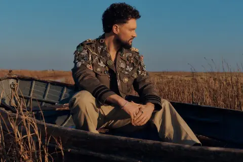 Calum Scott w łodzi, w kurtce ozdobionej broszkami, jakby śpiewał "You Are The Reason".