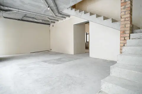 Wnętrze domu w stanie deweloperskim. Betonowe schody, ściany z tynkiem, widoczne instalacje i przewody.