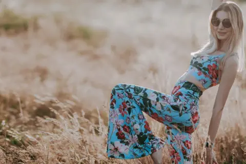 Blondynka w kwiecistym komplecie i okularach przeciwsłonecznych, uosobienie wolnego ducha i mody lat 70., pozuje na tle złocistego pola.
