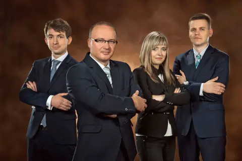 Cztery osoby w garniturach stojące z rękami skrzyżowanymi na piersi.