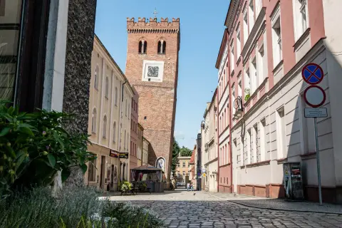 Wieża zegarowa w Ząbkowicach Śląskich na tle kamienic i brukowanej ulicy.