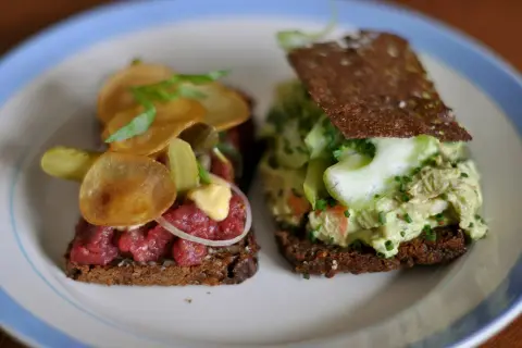 Dos sándwiches abiertos, uno con tartar de ternera y patatas fritas, otro con ensalada de pollo y pepino. Comida típica de Dinamarca.