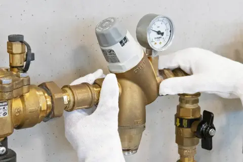 Mani guantate regolano un riduttore di pressione con manometro, mostrando come si regola la pressione dell'acqua.