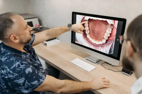 Dentysta pokazuje pacjentowi na ekranie komputera zdjęcie jamy ustnej, wskazując na zdrową kieszonkę dziąsłową.