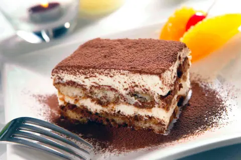 En bit krämig tiramisu, pudrad med kakao, serveras med frukt. Perfekt som dryck till tiramisu är kaffe eller en söt dessertvin.
