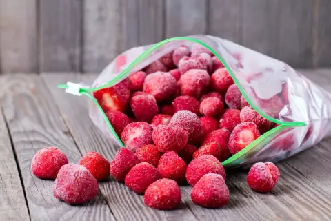 Mrożone truskawki wysypują się z otwartej torebki. Idealne, by rozmrażać truskawki do galaretki.
