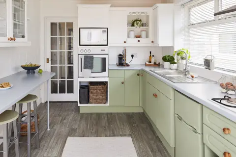 Cocina renovada con gabinetes verdes, encimeras grises y electrodomésticos blancos. Un espacio luminoso y funcional para tu reforma cocina.