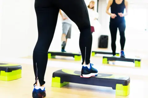 Kobieta w czarnych legginsach ćwiczy na stepperze w sali fitness.