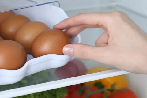 Dłoń wkłada jajka do wytłaczanki w lodówce. To prosty sposób, jak przechowywać jajka, by były świeże.