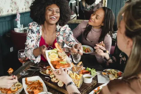 Vier Freundinnen genießen einen köstlichen Brunch in Berlin. Sie lachen und teilen sich Speisen wie Garnelen und Pommes.