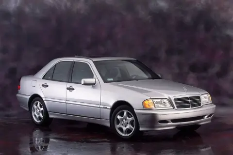 Srebrny Mercedes-Benz C-Klasa W202 z lat 90. na tle ciemnego, malowanego tła.