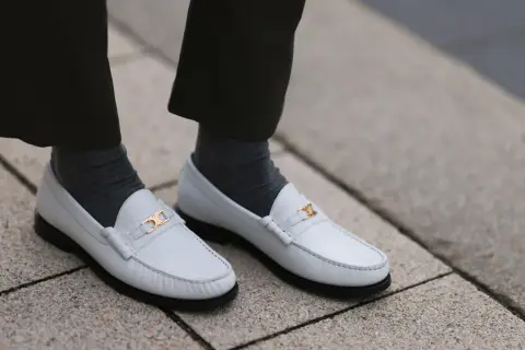 Scarpe pulite bianche con fibbia dorata, calzini grigi e pantaloni scuri.