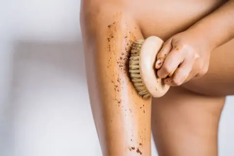 En hand använder en borste för att exfoliera benet med en brun skrubb. Det är ett bra sätt att få mjuk hud.