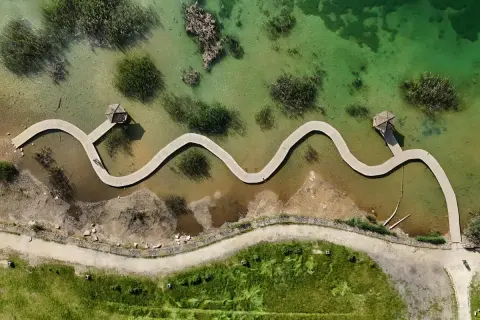 Malownicze polskie Malediwy z falującymi drewnianymi pomostami i altanami. Woda jest krystalicznie czysta, a otoczenie bujnie zielone.