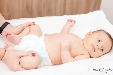 Delikatne ćwiczenia bioderek niemowlaka, by zapobiec dysplazji stawu biodrowego. Fizjoterapeuta delikatnie porusza nóżkami dziecka.