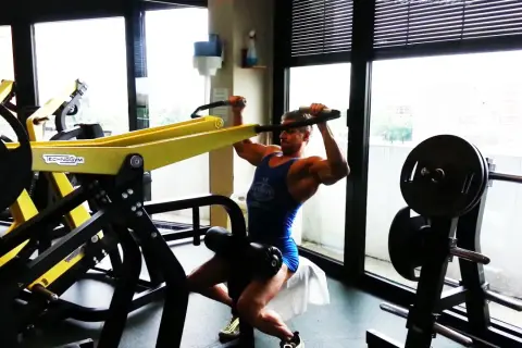 Uomo muscoloso esegue esercizi dorsali macchinari Technogym, concentrato sul movimento.