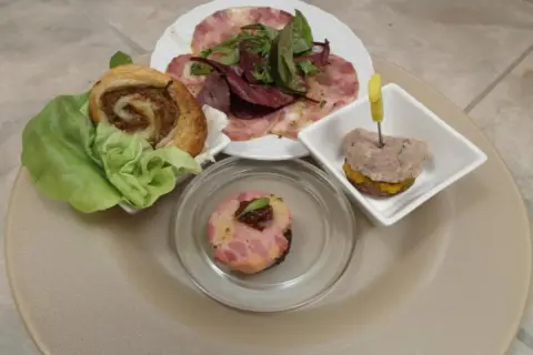 Verschiedene Tapas mit Fleisch: ein Fleischröllchen im Blätterteig, ein kleiner Burger mit Fleisch und ein Stück Fleischpastete.