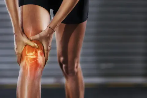 Eine Person hält ihr Knie, das rot leuchtet, um **Schmerzen unter der Kniescheibe** zu symbolisieren.