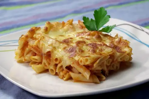 Un delicioso plato de macarrones al horno con queso gratinado y una hoja de perejil.
