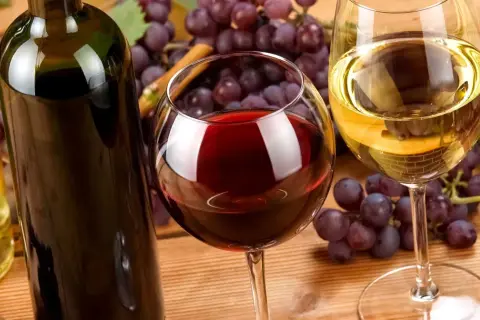 Butelka i kieliszki z winem, winogrona. Warto pamiętać o potencjalnych białym winie właściwości lecznicze.
