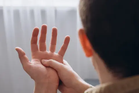 Mężczyzna masuje dłoń, odczuwając drętwienie rąk.
