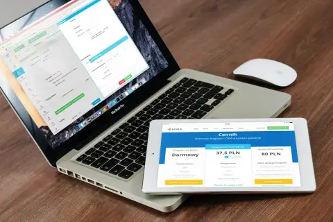 Programista .NET pracuje nad aplikacją na laptopie i tablecie. Na ekranach widoczne są formularze i cennik usług.