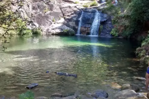 Un hombre disfruta de las pozas de Mougas, con cascadas cayendo sobre rocas y agua cristalina.