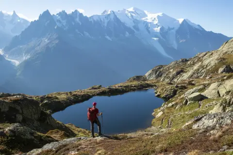 Widok na wejście na Mont Blanc. Turysta z plecakiem stoi nad górskim jeziorem, podziwiając ośnieżone szczyty.