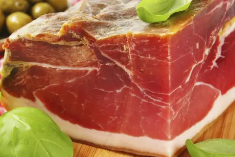 Ein Block Parma-Schinken mit zartem Fleisch und weißem Fett, garniert mit Basilikum. So sieht er aus, der echte Parma-Schinken.