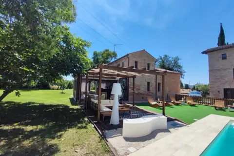 Un'oasi di relax a Poggio San Romualdo: piscina, prato verde, pergolato con divani e lettini prendisole.